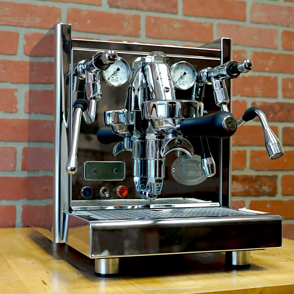 The (SOLD) SIDEWALK SALE - ECM Technika V Profi HX Espresso Machine shines on a wooden surface by a red brick wall—ideal for adding professional espresso style to your setup. © 2025 1st-line.com