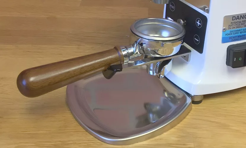 A portafilter with a wooden handle is attached to the Mazzer Mini B Electronic Time-Based Espresso Coffee Grinder, which rests on a shiny metal tray atop a wooden surface. © 2025 1st-line.com