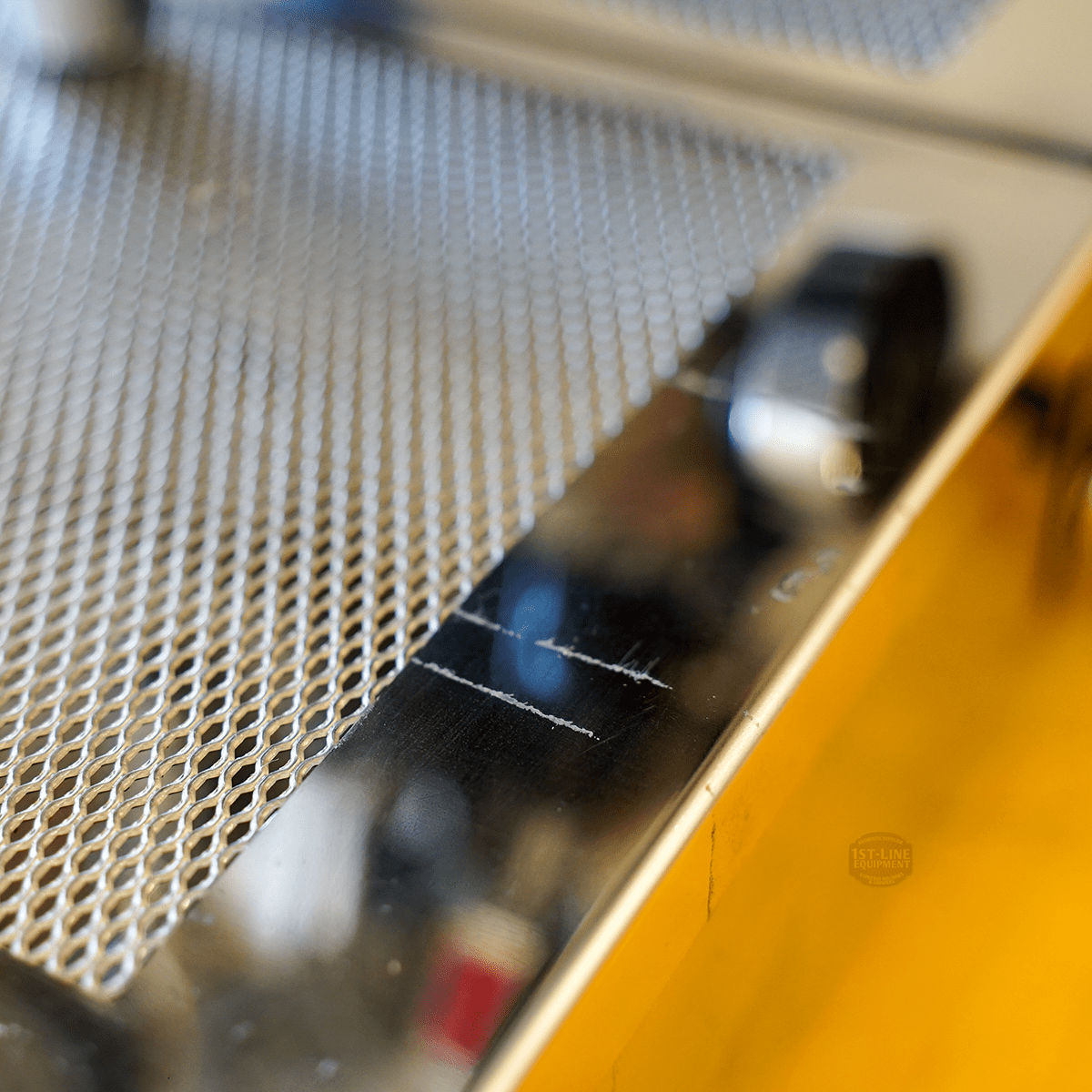 Close-up of a SIDEWALK SALE - VBM Domobar Super HX Switchable Espresso Machine OPEN BOX (E110) metal surface shows its perforated grid and scratched shiny edge, with blurred background and lighting that highlights the metallic texture. © 2025 1st-line.com
