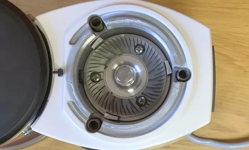 Close-up of the Mazzer Mini B Electronic Time-Based Espresso Coffee Grinder, showing its metal burr grinding mechanism with three screws inside a white plastic base, placed on a wooden surface. © 2025 1st-line.com