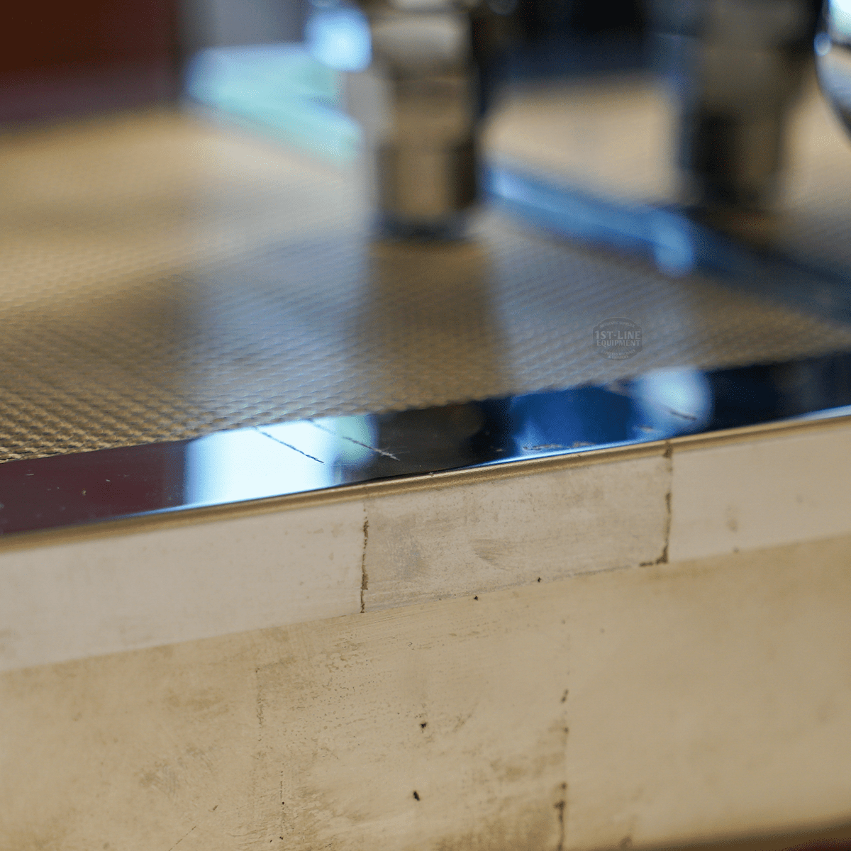 Close-up of the shiny, textured surface and sleek edge of the SIDEWALK SALE - VBM Domobar Super HX Switchable Espresso Machine OPEN BOX (E110); blurred metal fittings in the background evoke an industrial vibe. © 2025 1st-line.com