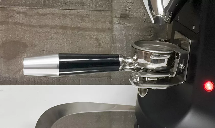 A close-up of a portafilter on an espresso machine with a red indicator light, set against dark wood and metal, with a Mazzer Super Jolly V Pro Espresso Coffee Grinder nearby. © 2025 1st-line.com
