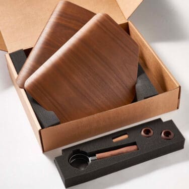 Open cardboard box with the VBM WOODENKITDS Domobar Super Wood Kit: two wooden boards, foam insert with metal and wood-handled scoop, two round wooden pieces, and a small wooden stick. © 2025 1st-line.com
