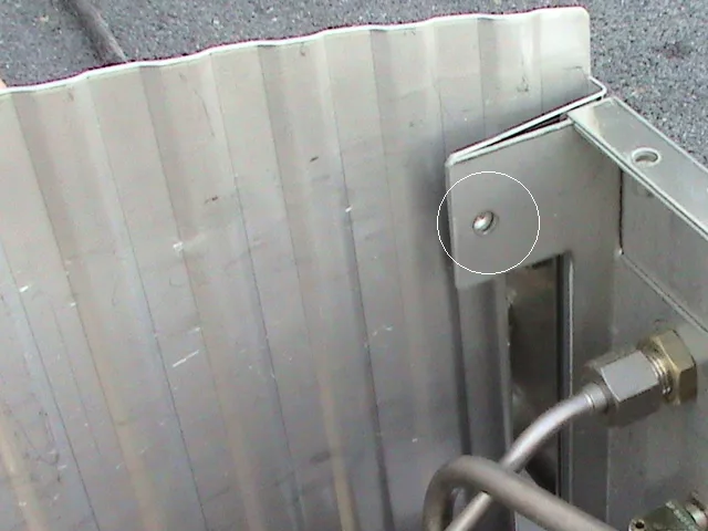 Close-up of a corrugated metal panel with a bolt and attached pipe fittings, highlighting a small dent or imperfection circled on the surface—similar to detailing found on Fiorenzato Bricoletta espresso machine components. © 2025 1st-line.com