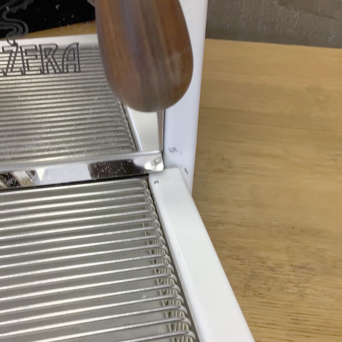 Close-up of a RETURNED & REFURBISHED Bezzera Aria HX Special Edition Espresso Machine w/ Flow Control (C104), featuring a wooden handle and metal drip tray on a light wood countertop. Brand name partially visible on the left. © 2025 1st-line.com