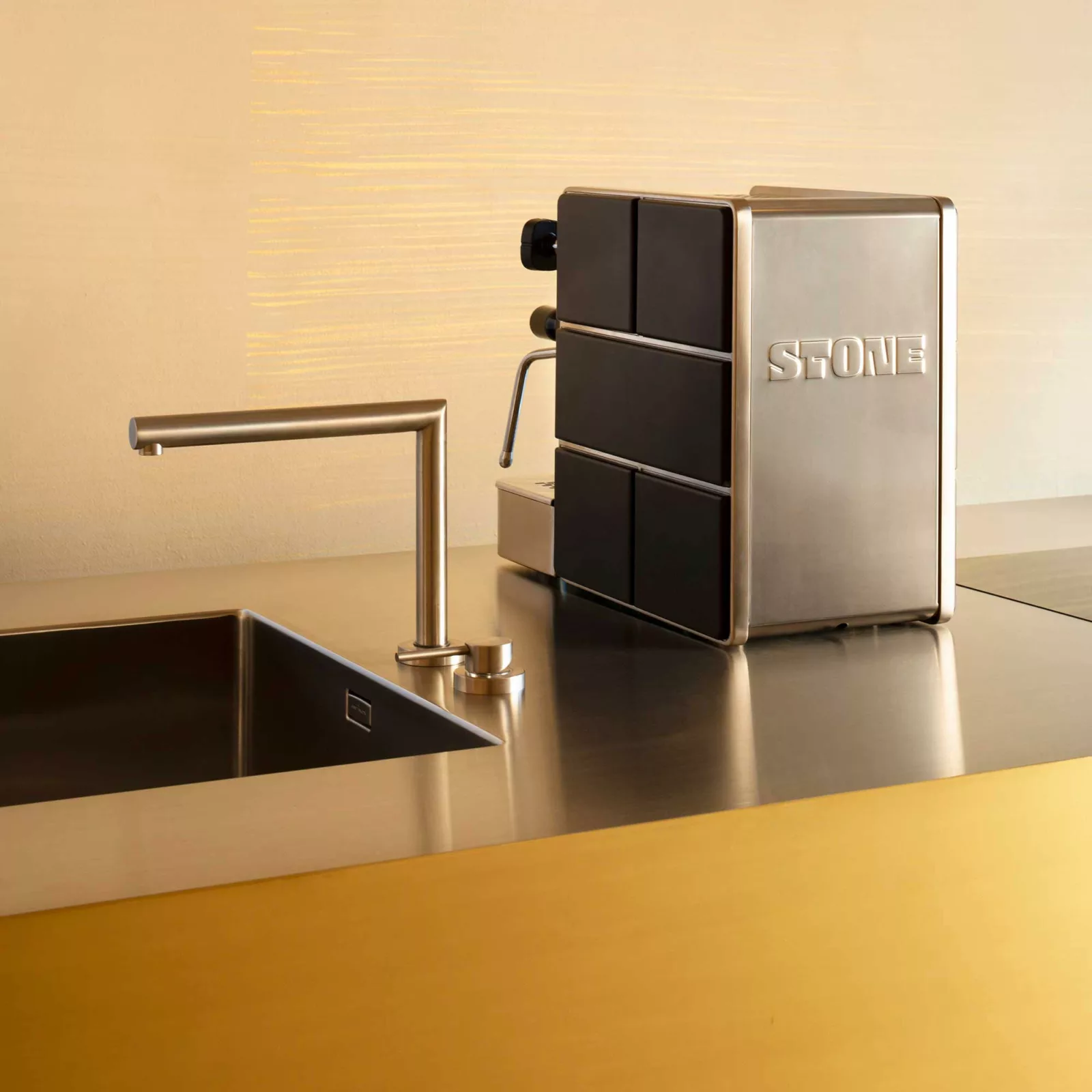 The Stone HX Espresso Machine, crafted from stainless steel, sits on a sleek metallic countertop beside a minimalist sink and matching faucet, bringing a contemporary feel to the kitchen. © 2025 1st-line.com