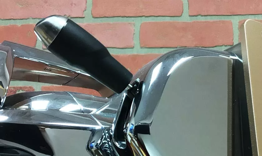 A close-up of the chrome lever and portafilter handle on the Faema Faemina Dual Boiler Espresso Machine, set against a red brick wall. © 2025 1st-line.com