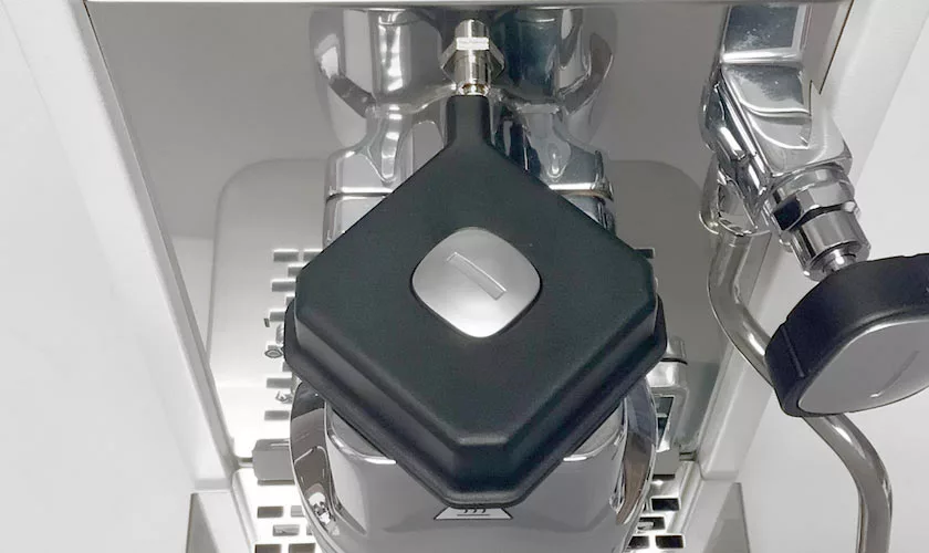 A close-up of the Stone HX Espresso Machine shows a black, square-shaped blind filter on the portafilter, used for cleaning or backflushing the machine. © 2025 1st-line.com