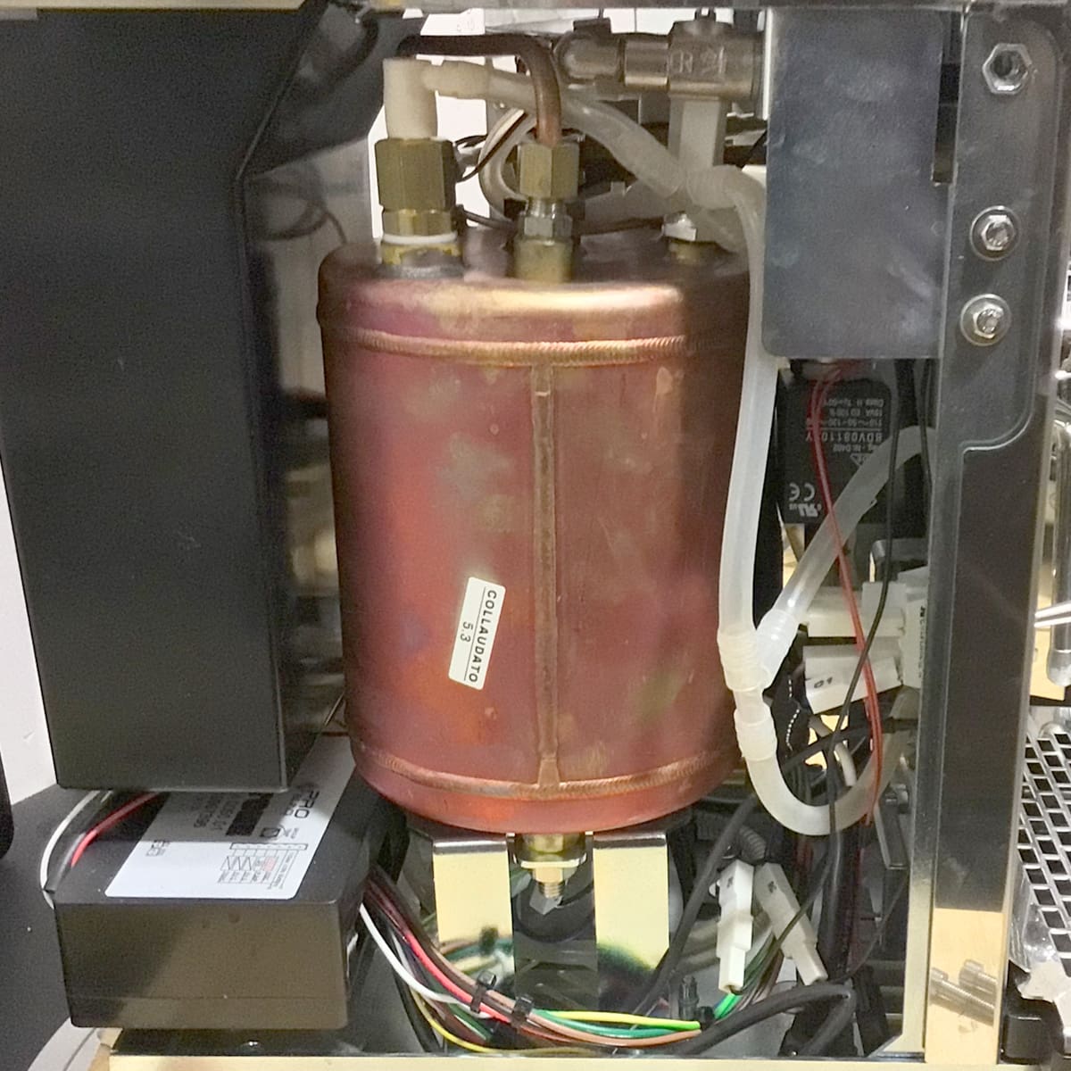 A close-up view inside the Stone HX Espresso Machine showcases its cylindrical copper boiler with connecting pipes and wires, along with surrounding mechanical and electronic components. © 2025 1st-line.com