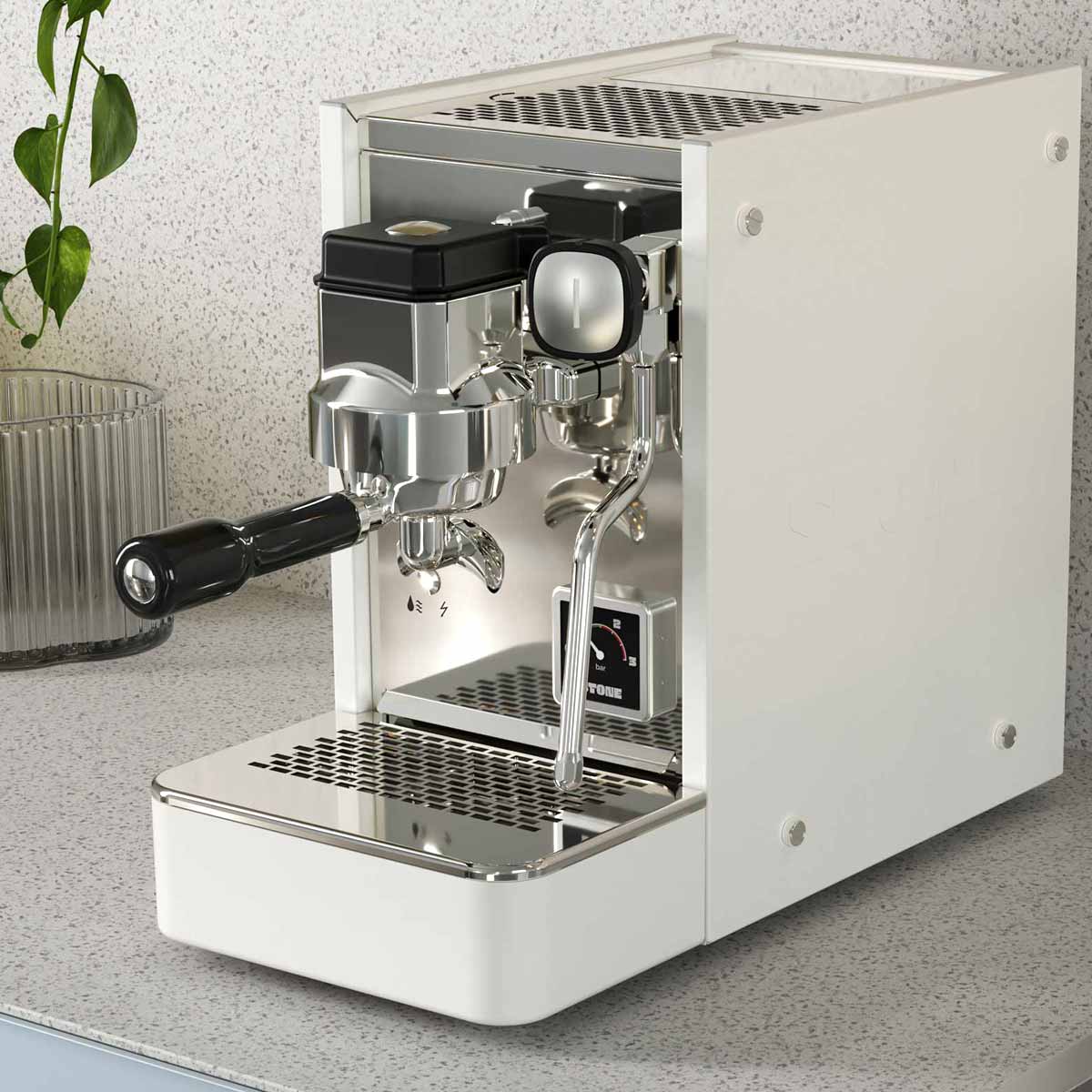 A white Stone HX Espresso Machine with a portafilter and digital gauge sits on a light gray kitchen countertop near a clear glass, a green trailing plant, and the sleek Stone HX Coffee Maker. © 2025 1st-line.com