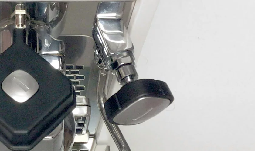 Close-up of a Stone HX Espresso Machine with portafilter handle attached; a tamper and steam wand are also visible. The background is mostly white. © 2025 1st-line.com