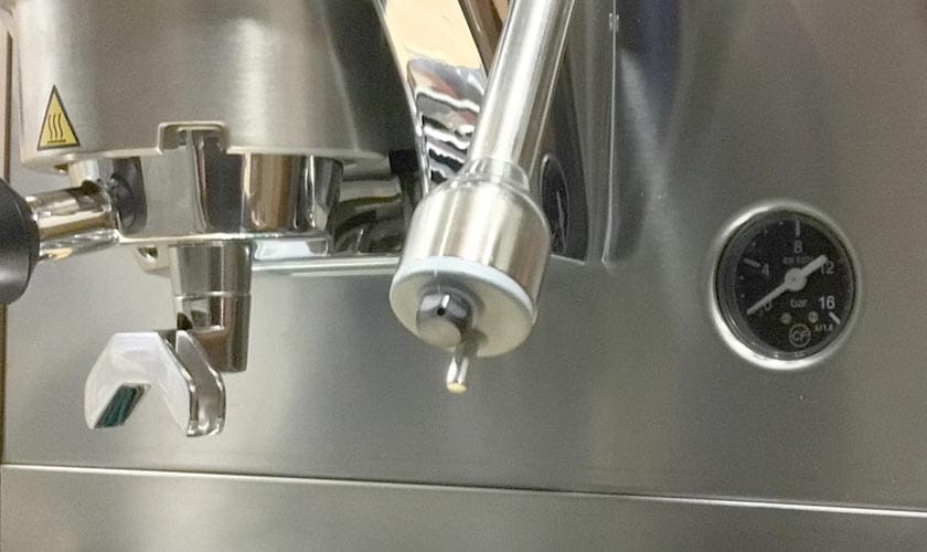 Close-up of the Faema Faemina Dual Boiler Espresso Machine, highlighting its portafilter, steam wand, pressure gauge, and caution sign against a gleaming stainless steel finish. © 2025 1st-line.com