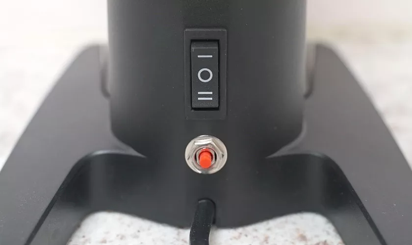 Close-up of the Pinecone Pinion All-Purpose Espresso Coffee Grinder in black, showing a power switch with I/O symbols and a red push button below, mounted on a stand with a cable extending from the base. © 2025 1st-line.com