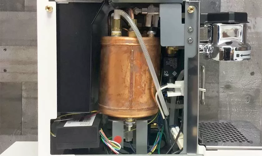 Close-up of the Stone HX Espresso Machine’s interior, featuring a large copper boiler, tubes, wires, and metal components with the casing partially open to reveal its internal parts. © 2025 1st-line.com