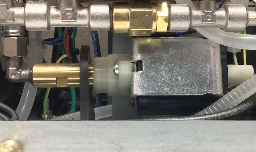 Close-up view of mechanical and electrical components inside the Stone HX Espresso Machine, featuring metal pipes, connectors, a cylindrical brass part, and various wires and tubes. © 2025 1st-line.com