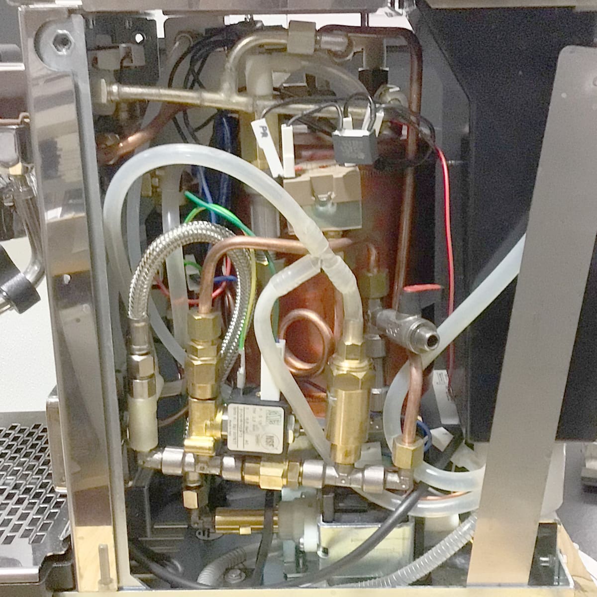 The image displays the internal components of the Stone HX Espresso Machine, featuring tightly arranged tubes, wires, brass fittings, and metal parts within its open metal casing. © 2025 1st-line.com