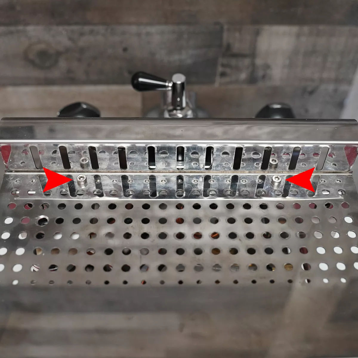 A close-up of a VBM Domobar espresso machine drip tray with two red arrows pointing to screws on the slotted back panel above the perforated tray. © 2025 1st-line.com