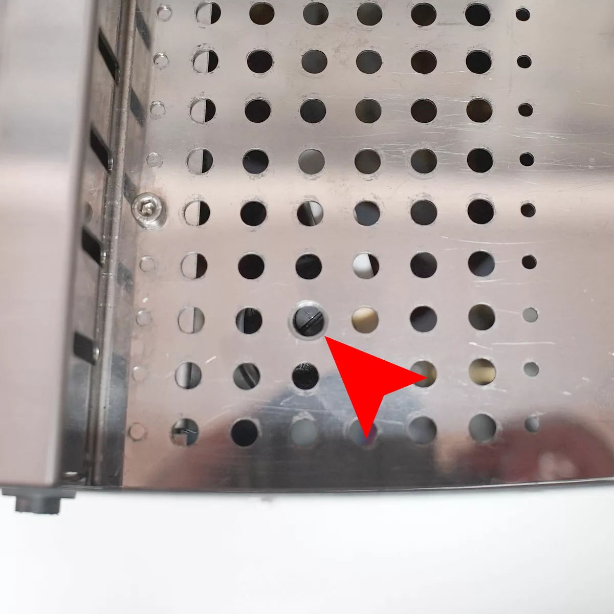 A red arrow points to a small, black screw inside the metal panel of a VBM Domobar Super espresso machine, with regularly spaced round holes. © 2025 1st-line.com