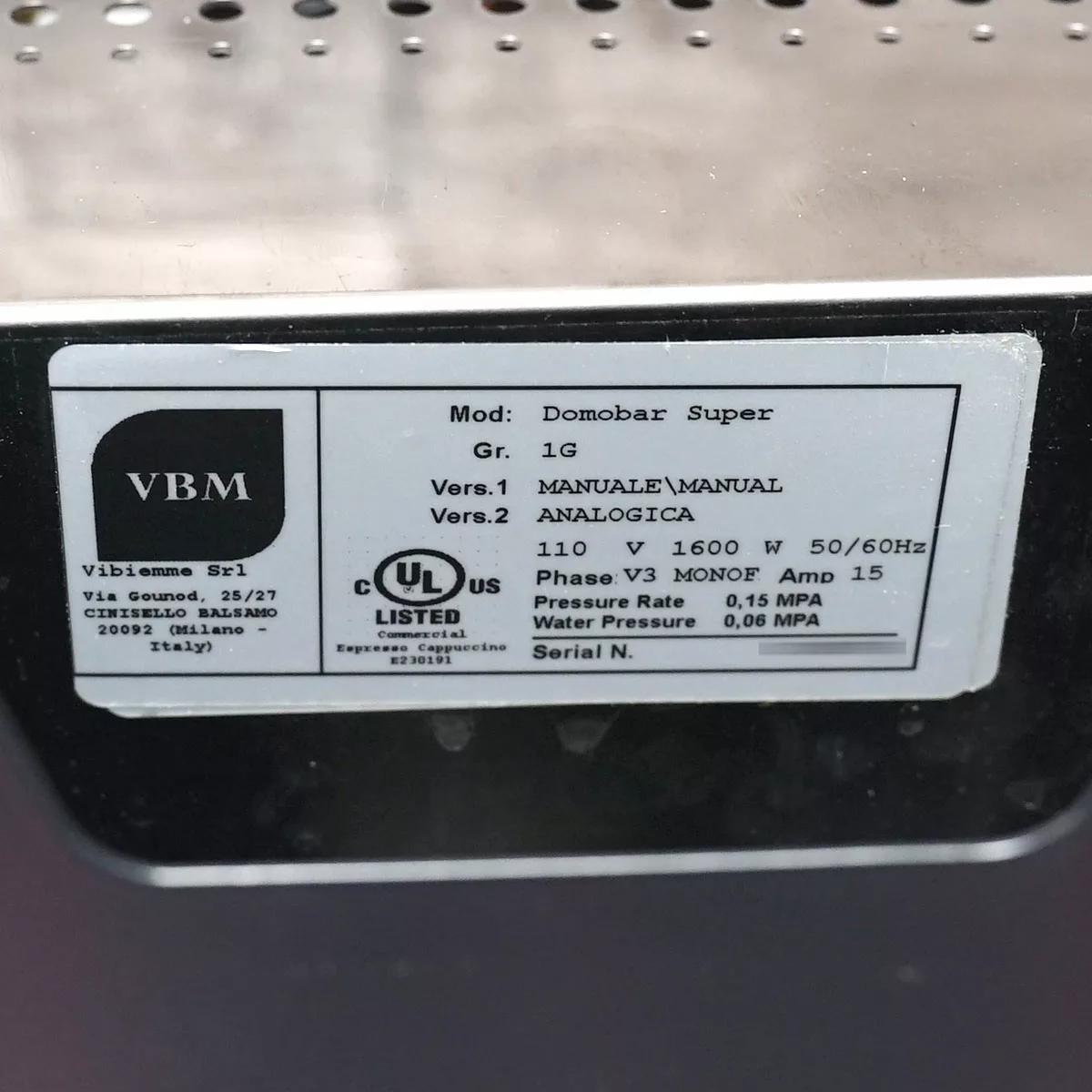 Close-up of a metal label on the VBM Domobar Super Analogic espresso machine, displaying technical specifications such as voltage, power, pressure, and manufacturer details in black and white text. © 2025 1st-line.com