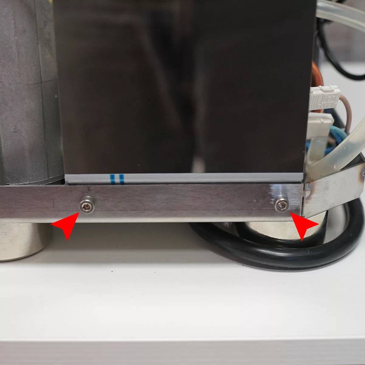 Close-up of a metal panel secured by two screws, highlighted by red arrows on a VBM Domobar espresso machine, with wires and components visible in the background. © 2025 1st-line.com