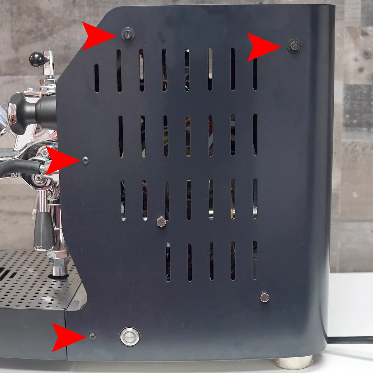 Side view of a black VBM Domobar espresso machine with red arrows pointing to screws and key areas on the metal panel, possibly indicating spots to remove for maintenance or repair. © 2025 1st-line.com