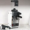 A white Slingshot Dosis S75 Espresso Coffee Grinder (CONVENTION DEMO, 220V) with a transparent bean hopper sits on the countertop, its power cord and plug coiled neatly beside it. © 2025 1st-line.com