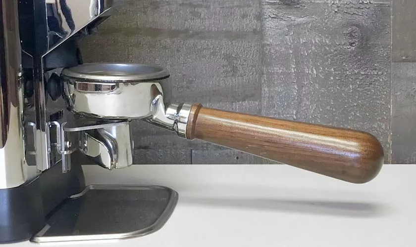 A close-up of a Faema espresso machine with a wooden-handled portafilter on a white countertop, set against a gray textured wall, alongside the Faema TOUCH & MATCH Espresso Coffee Grinder. © 2025 1st-line.com