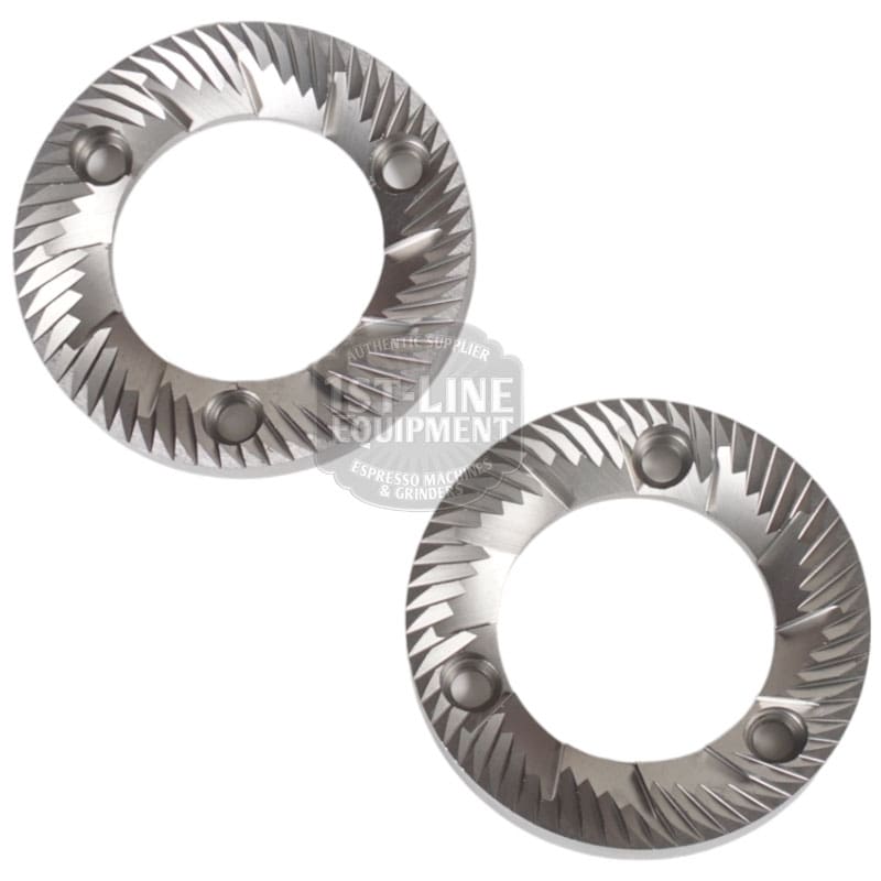 A set of two Quamar 260015 63 mm Grinding Burrs, each circular and metallic with three screw holes, are slightly overlapping on a white background. © 2025 1st-line.com