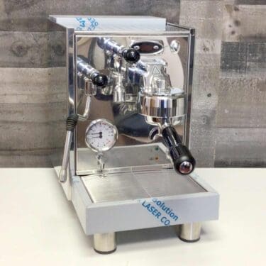 A shiny SIDEWALK SALE - Bezzera BZ07 V1 PM PID Espresso Machine (demo, E112) with pressure gauge, steam wand, and portafilter sits on a white surface against a gray wooden wall background. © 2025 1st-line.com