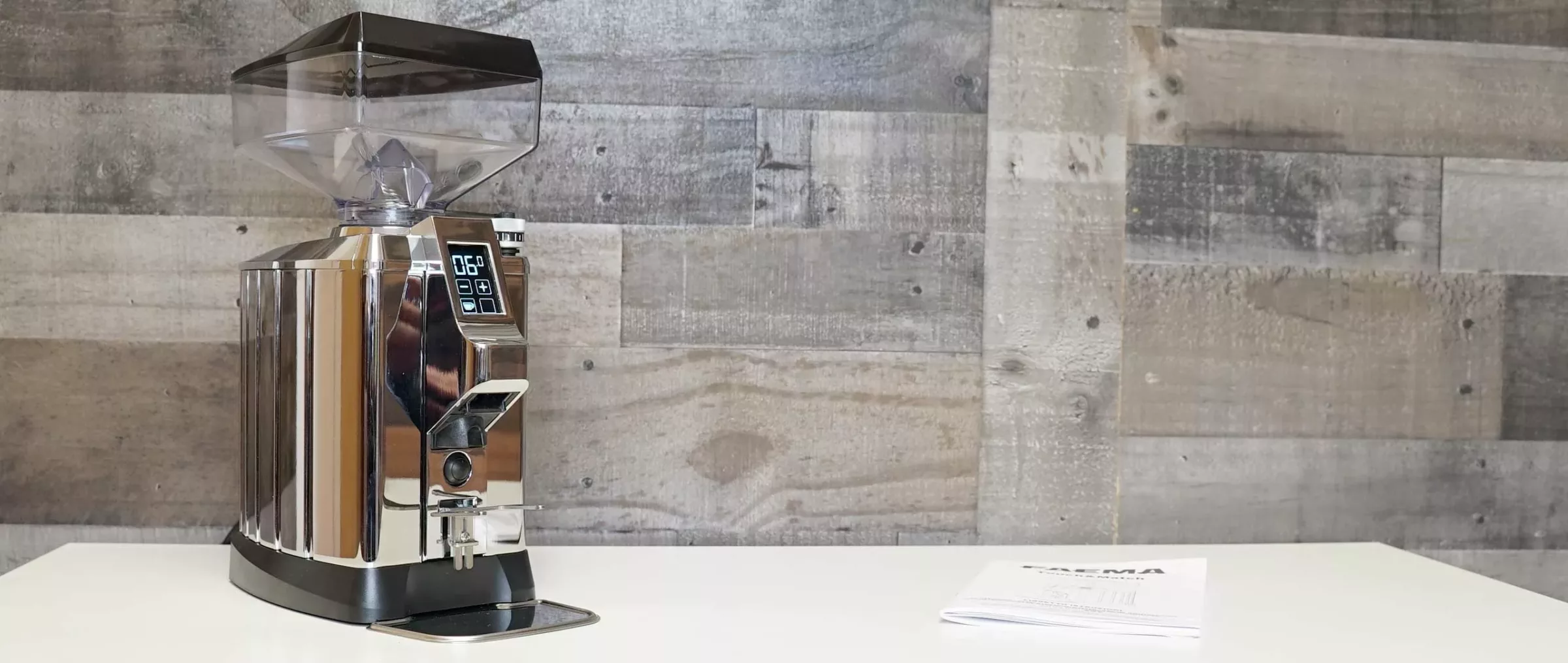 A sleek Faema TOUCH & MATCH Espresso Coffee Grinder sits on a white counter with its user manual beside it, set against a wall of light and dark wood panels that highlight its modern design. © 2025 1st-line.com