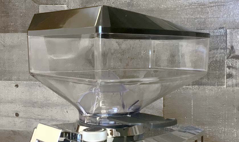 Close-up of an empty, transparent plastic hopper on a Faema TOUCH & MATCH Espresso Coffee Grinder, set against a wooden background in varying shades of gray. © 2025 1st-line.com