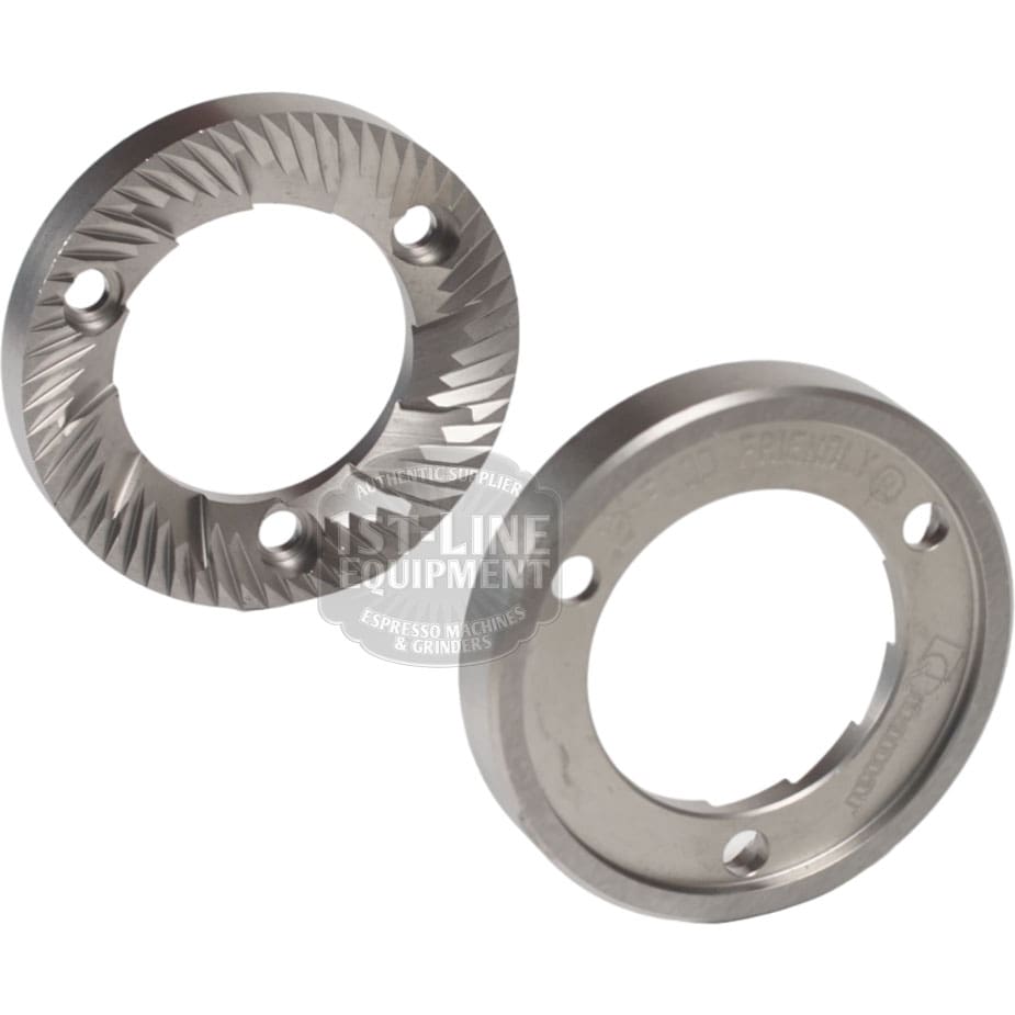 The Quamar 260015 63 mm Grinding Burrs set includes two circular, silver grinding burrs with sharp, angled teeth and multiple screw holes, designed for Quamar coffee grinders and shown against a white background. © 2025 1st-line.com