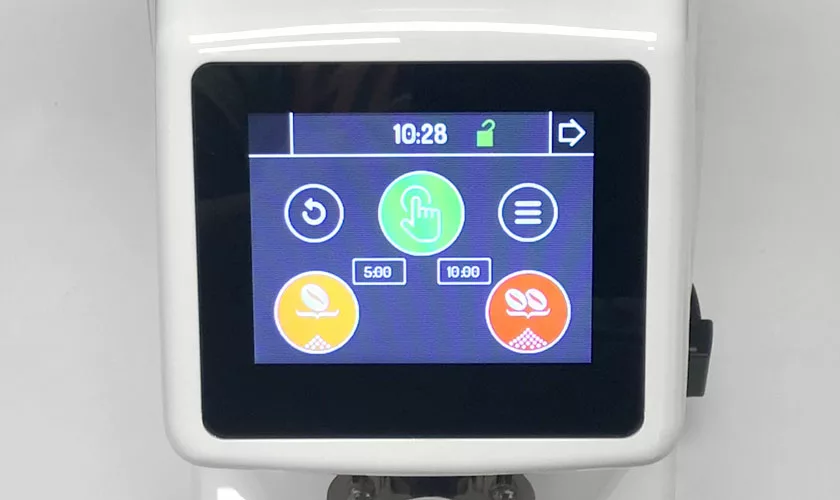 The Quamar M80TP Espresso Coffee Grinder features a touchscreen with icons for power, menu, and two plant settings, a large central green button, and the time 10:28 displayed at the top. © 2025 1st-line.com