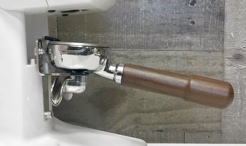 A close-up of a coffee machine with a wooden-handled portafilter locked in place sits beside a Quamar M80TP Espresso Coffee Grinder, all set against a wooden-textured background. © 2025 1st-line.com