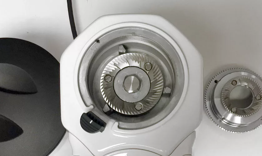 Close-up of the Quamar M80TP Espresso Coffee Grinder in white with its top burr exposed, showing sharp grinding blades. The black lid and a separate metal burr are placed next to the grinder on a white surface. © 2025 1st-line.com