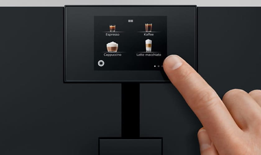A hand selects from Espresso, Kaffee, Cappuccino, and Latte macchiato options on the touchscreen of the Jura ENA 8 Super-Automatic Espresso Machine. © 2025 1st-line.com