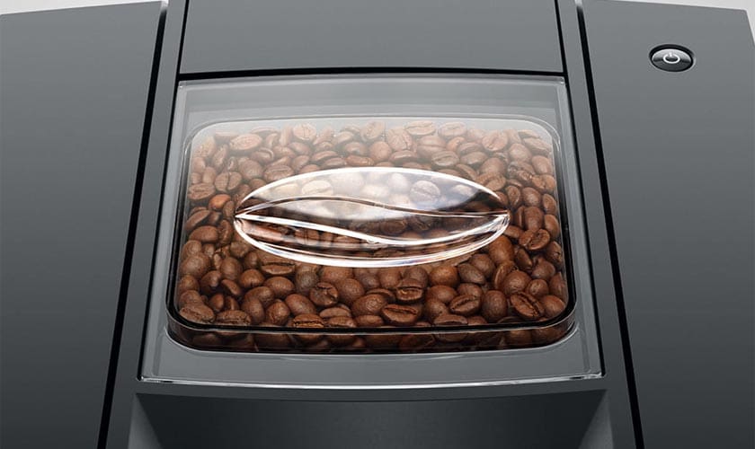 Close-up of a transparent container filled with roasted coffee beans, integrated into the sleek Jura E6 Super-Automatic Espresso Machine. © 2025 1st-line.com
