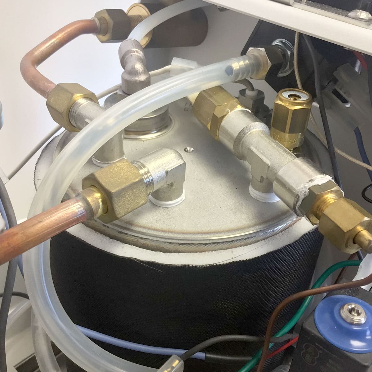 A close-up of the Nurri R-Type SB (HX) Espresso Machine shows metal pipes, brass fittings, clear plastic tubes attached to a cylindrical container with black insulation, visible wires, valves, and HX components. © 2025 1st-line.com