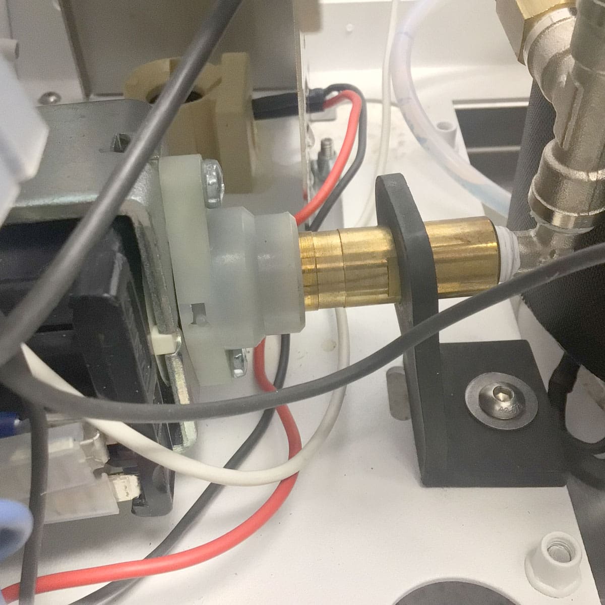 Close-up of an internal mechanical component inside the Nurri R-Type SB (HX) Espresso Machine: a brass cylinder linked to a gray plastic fitting with nearby white and red wires, highlighting its essential role in the machines design. © 2025 1st-line.com