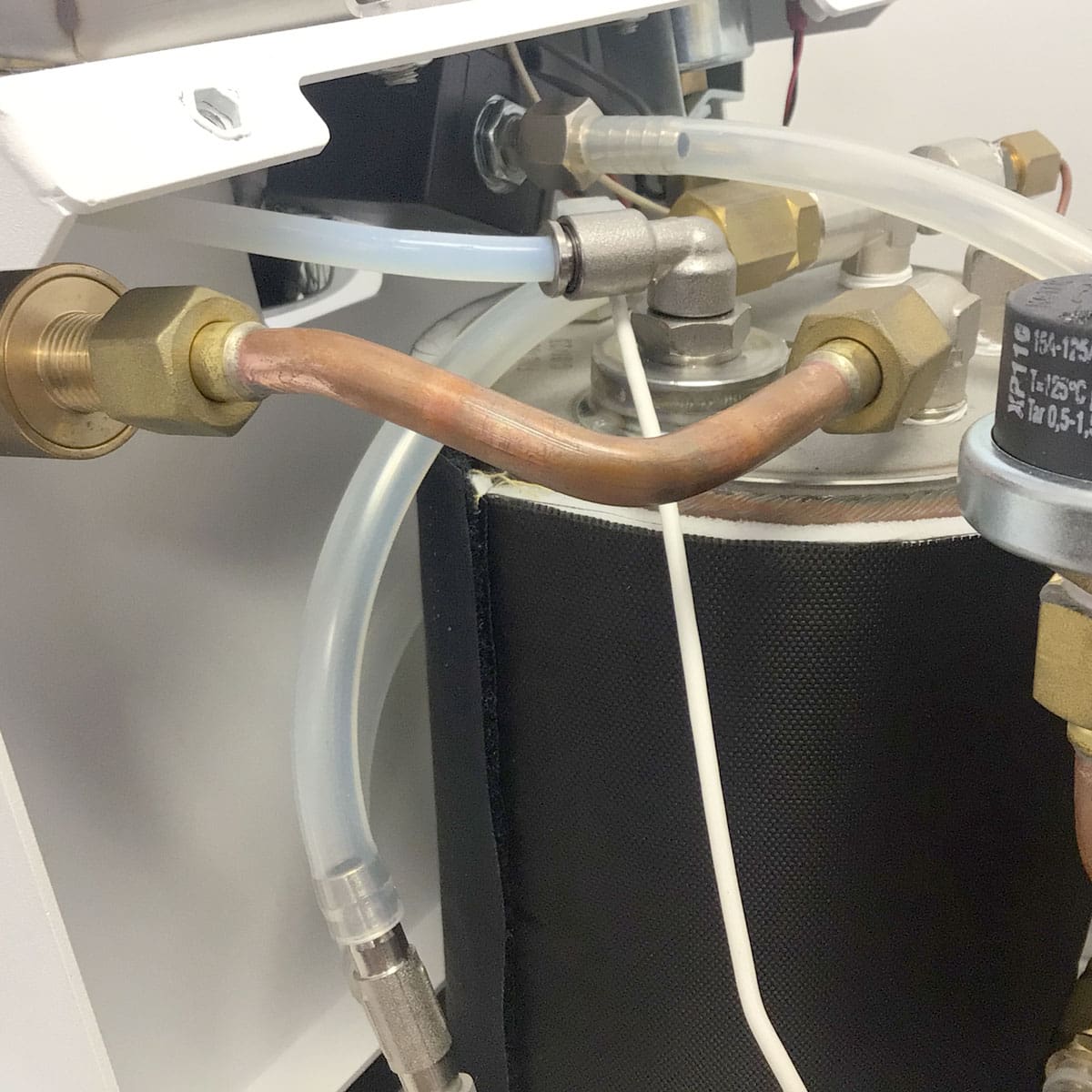 Close-up of copper pipes and clear plastic tubes connected to metal fittings on a cylindrical component inside a Nurri R-Type SB (HX) Espresso Machine, likely part of its water or heating system. © 2025 1st-line.com