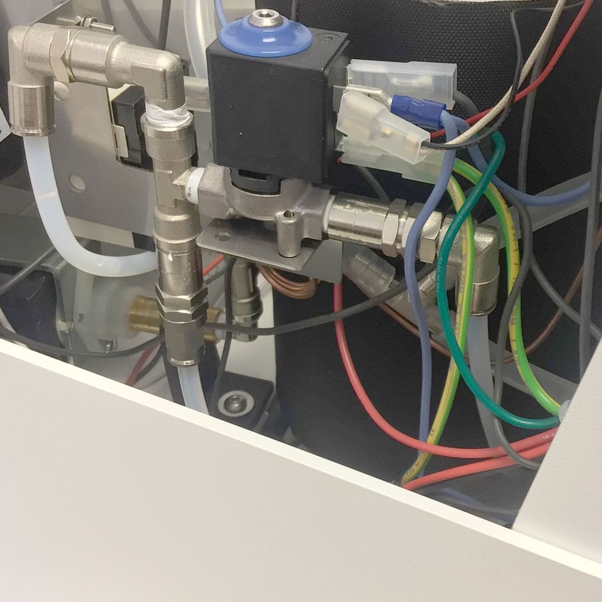 Close-up of industrial machine components in a white enclosure—metal pipes, blue-capped valve, wiring, connectors—reflecting the precision engineering of the Nurri R-Type SB (HX) Espresso Machine. © 2025 1st-line.com