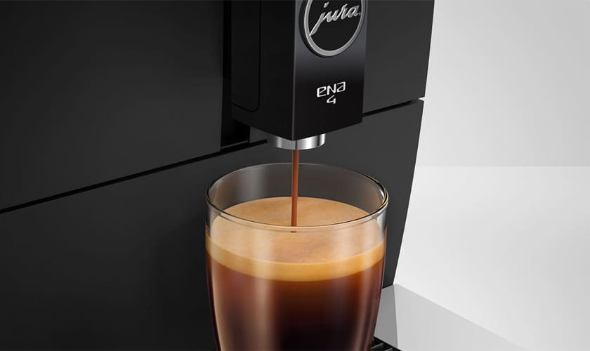 The Jura ENA 4 Super-Automatic Espresso Machine dispenses espresso into a clear glass, showcasing a rich layer of crema atop the freshly brewed coffee. © 2025 1st-line.com