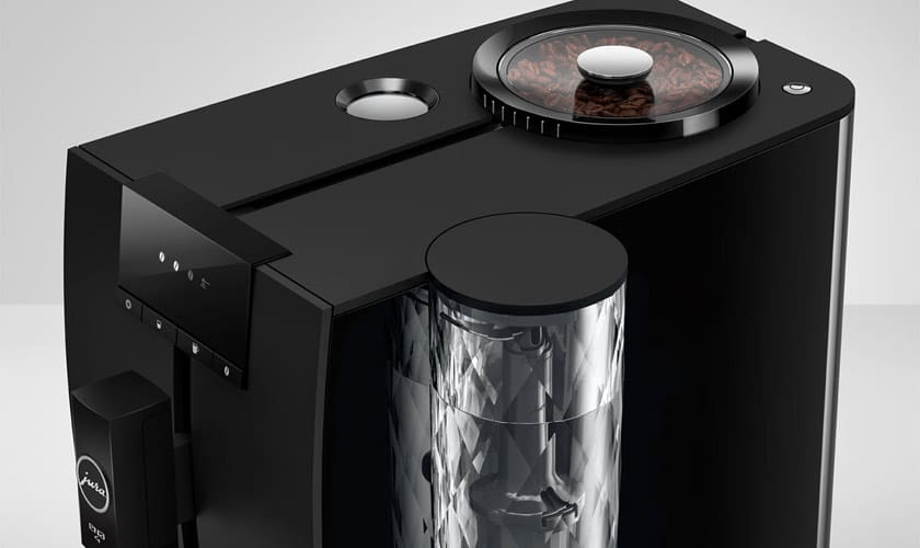The Jura ENA 4 Super-Automatic Espresso Machine in black features a visible coffee bean hopper and a transparent water reservoir, displayed on a light gray background. © 2025 1st-line.com