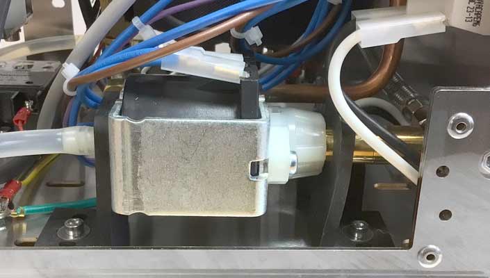 Close-up of an internal component from a Torre Alfredo TSP HX Espresso Machine, featuring a metal casing, white plastic connector, and several colored wires and tubes attached. © 2025 1st-line.com