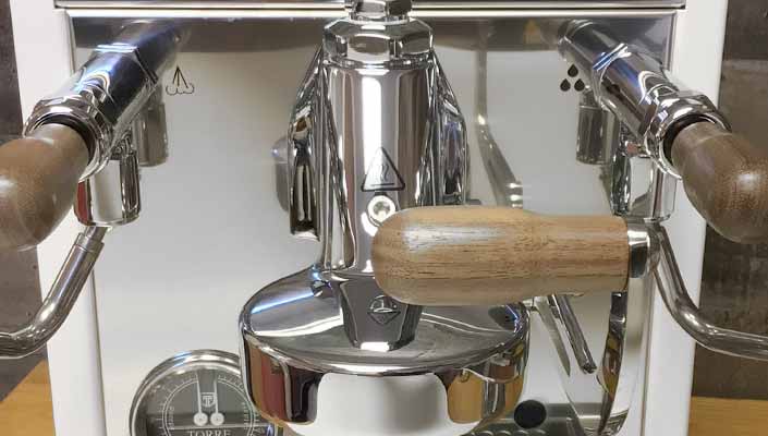 Close-up of the Torre Alfredo TSP HX Espresso Machine, showcasing its chrome and wood lever with a wooden handle, metal components, and a pressure gauge at the bottom left. © 2025 1st-line.com