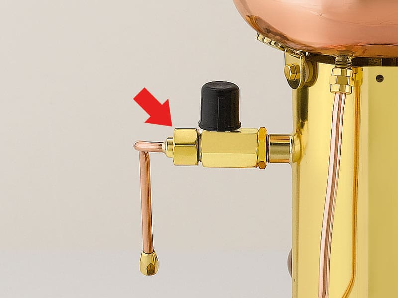 A red arrow points to a brass valve with a black knob on an Elektra Semi-Automatica, a gold and copper device, possibly highlighting a feature or step in repackaging the coffee machine. © 2025 1st-line.com