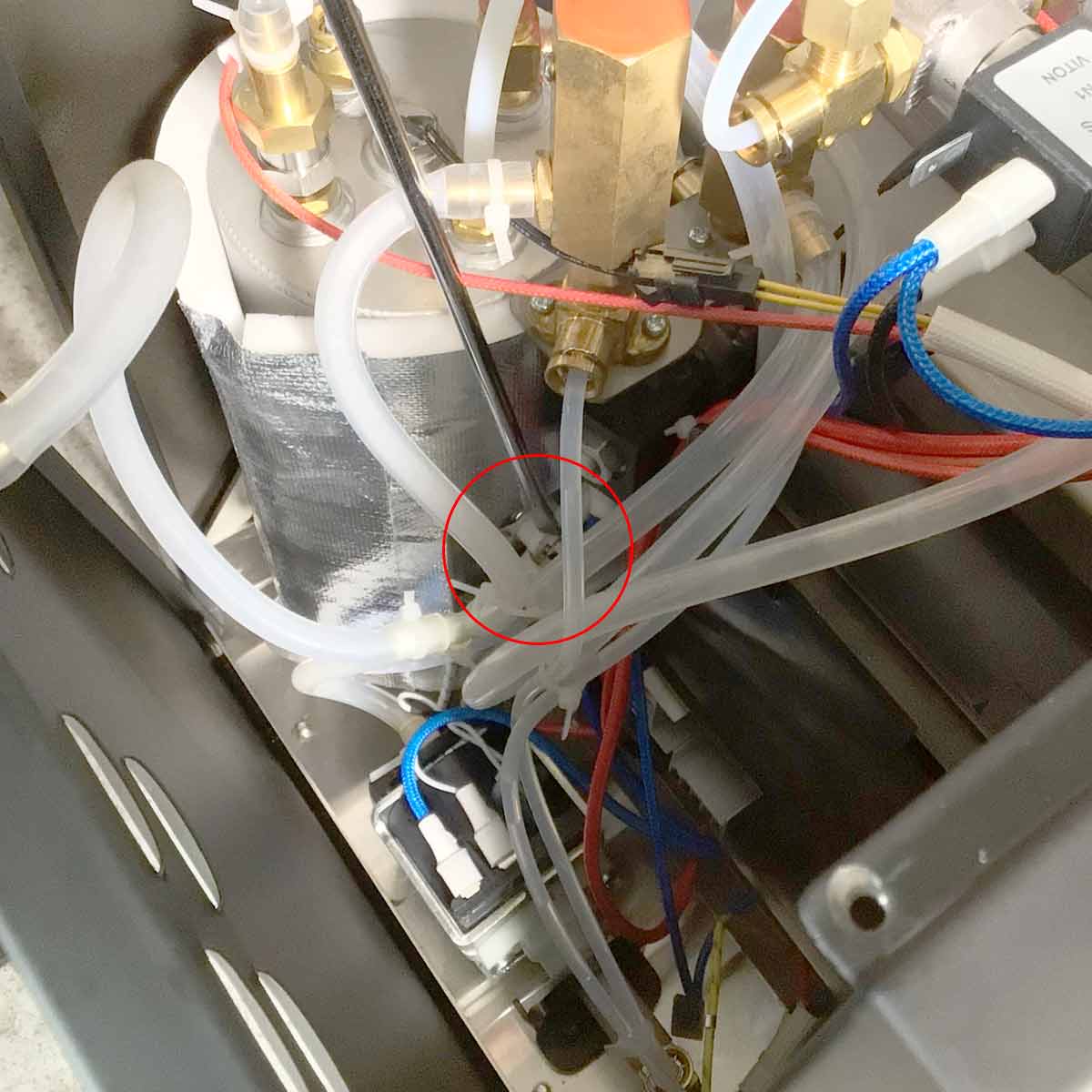 Close-up of an intricate machine interior with various clear tubes, wires, and metal components; a red circle highlights a specific connector among the tubes. © 2025 1st-line.com