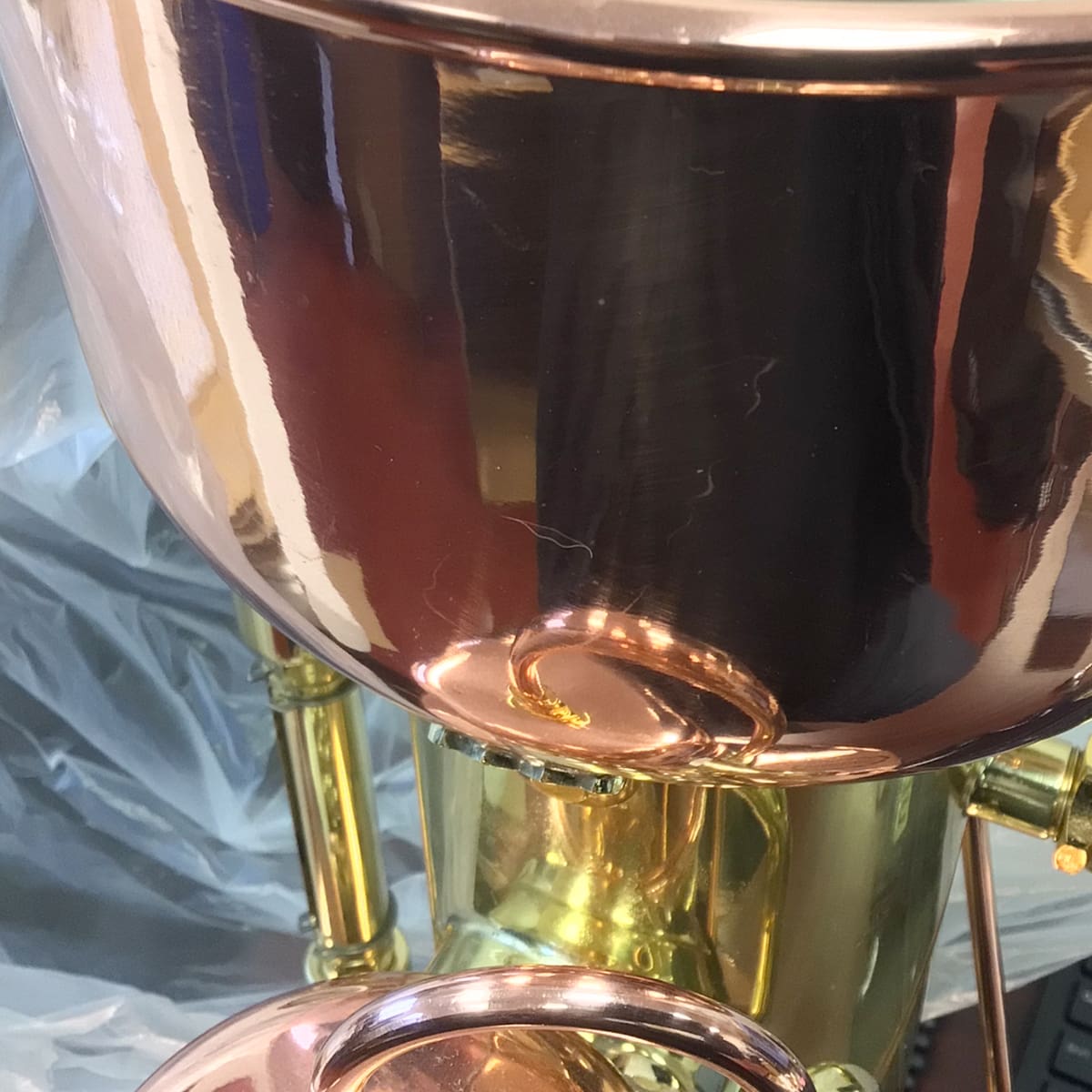 A close-up of a SIDEWALK SALE - Elektra SX Microcasa Semiautomatica Espresso Machine RETURNED & REFURBISHED (E211) with polished brass or copper, shiny metallic surfaces, and pipes, set against crinkled plastic.