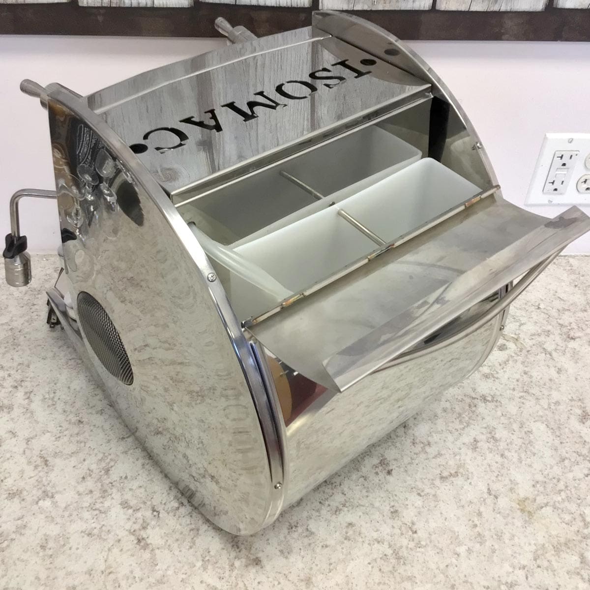 A shiny Tosmac ice cream or gelato machine with an open lid, showing white containers inside, sits on a speckled countertop near a wall outlet beside a SIDEWALK SALE - Isomac Mondiale HX Espresso Machine (E013). © 2025 1st-line.com