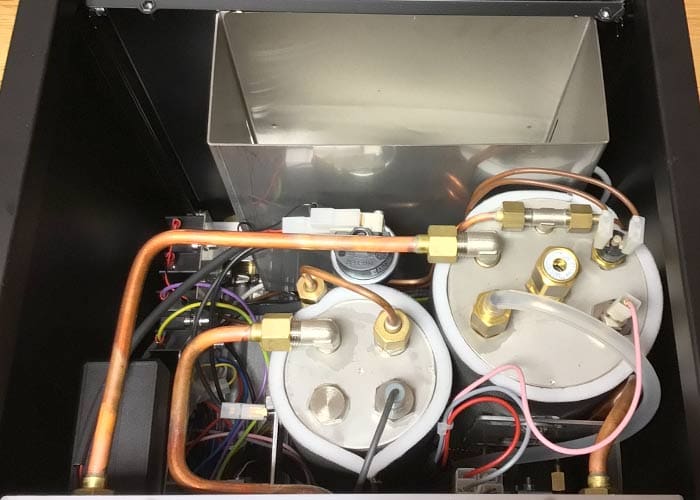 Inside view of the Torre Mariuccia Dual Boiler Espresso Machine w/ Flow Control, revealing two cylindrical metal boilers, copper pipes, wires, connectors, and valves that showcase its internal components and flow control system. © 2025 1st-line.com